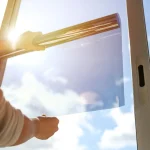 Person applying transparent film to window on sunny day.
