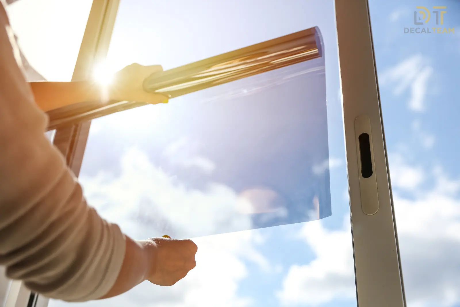 Person applying transparent film to window on sunny day.